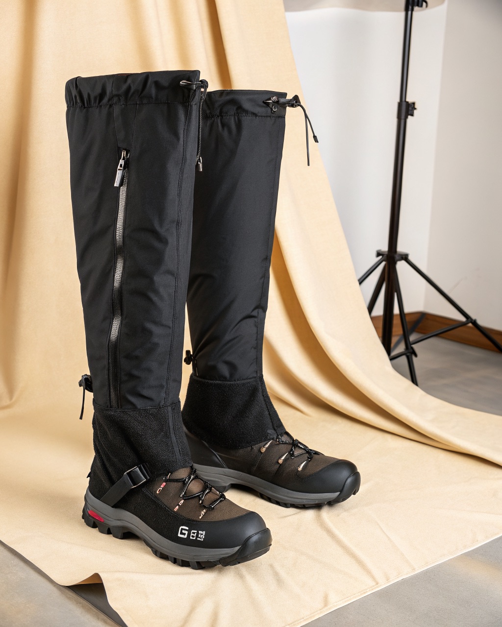 Pair of black knee-high gaiters standing upright showing the front hook-and-loop closure, lace hook, and steel instep cable underneath