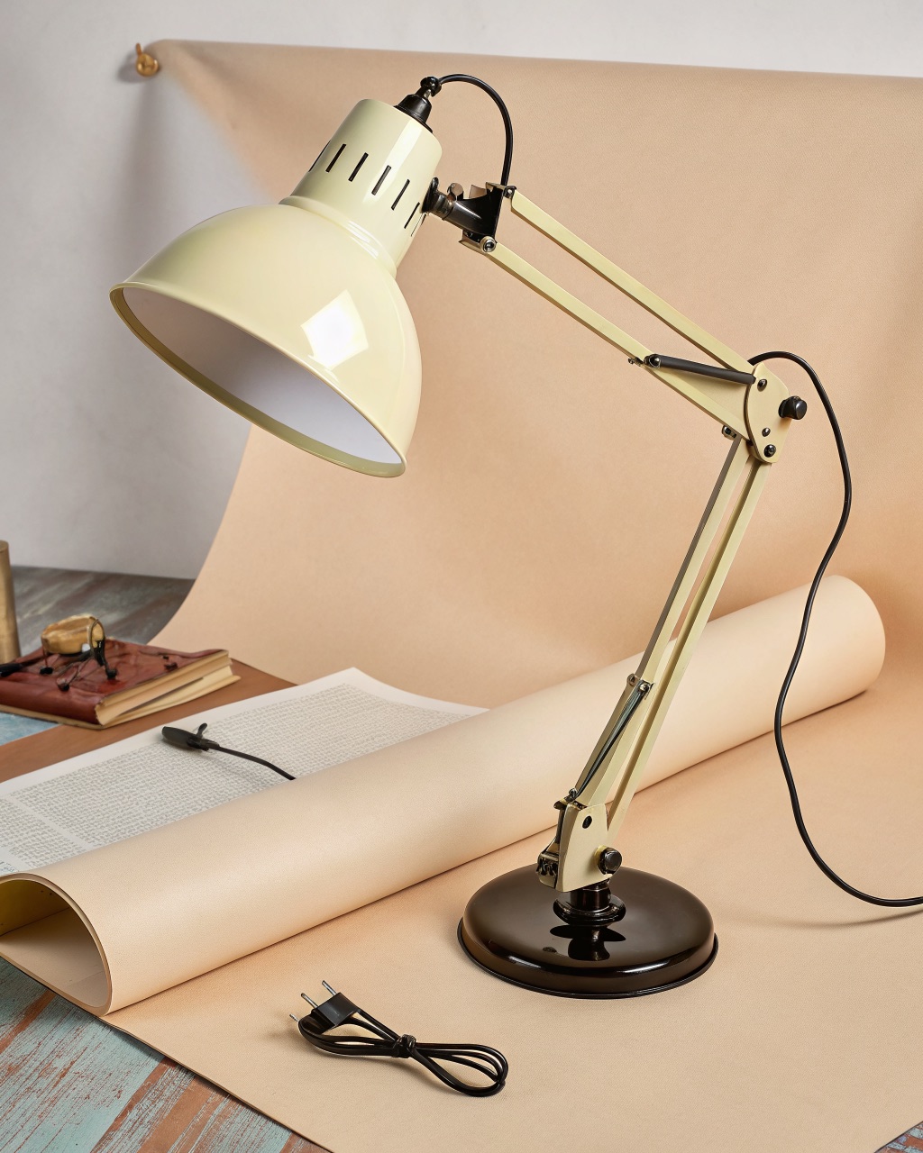 Pale yellow spring-balanced two-section task lamp on a heavy round cast-iron base, arm extended over a desk