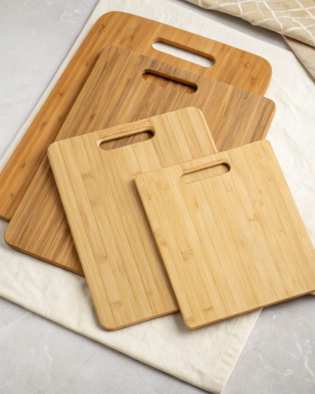 Three pale golden bamboo cutting boards in graduated sizes, fanned out to show the routed juice grooves