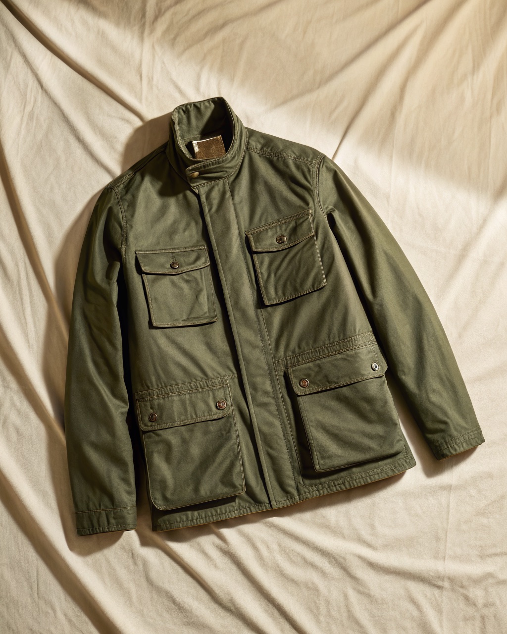 Olive waxed cotton canvas field jacket laid flat, showing the four patch pockets and snap placket