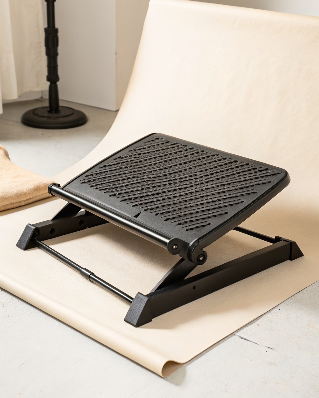 Black powder-coated steel under-desk footrest with a ridged tilting platform set at an angle on a floor