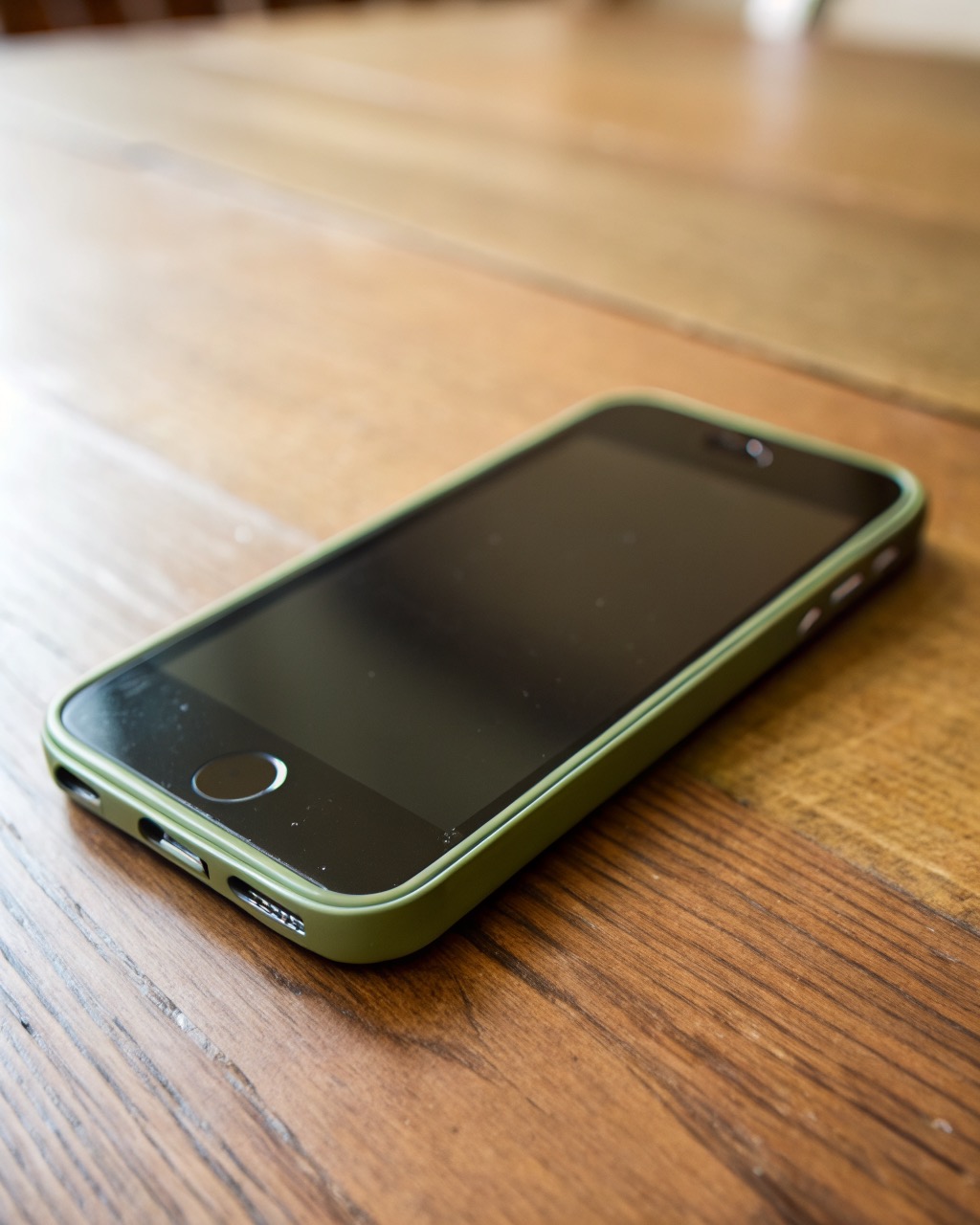 Small olive-green smartphone held in one hand, compact body with rounded edges, dual rear camera, dark screen, completely unbranded with no logos