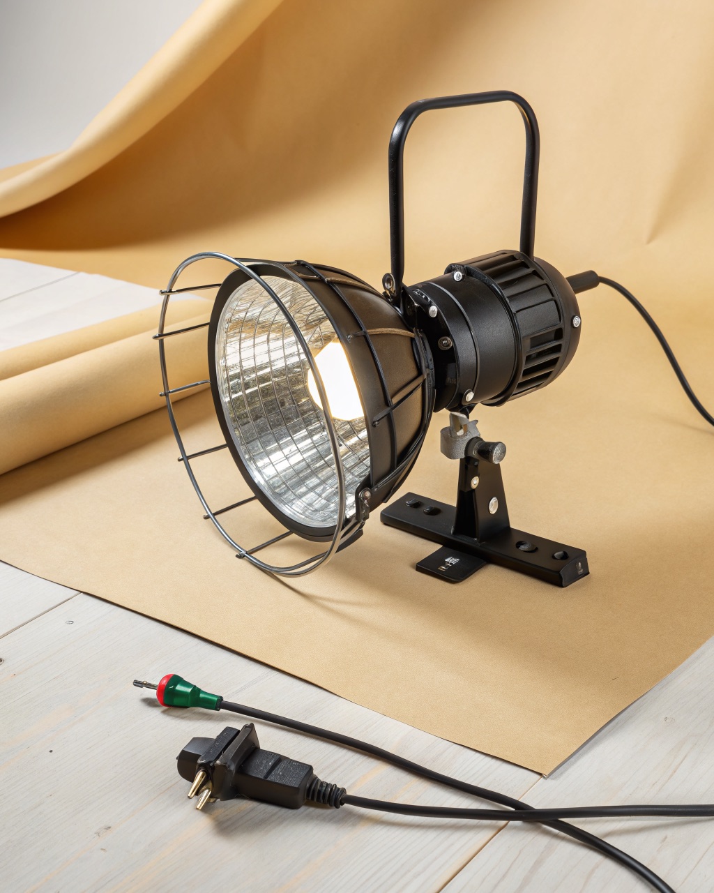 Aluminum reflector dome work light with a steel wire bulb guard mounted on a heavy spring clamp gripping a workbench edge