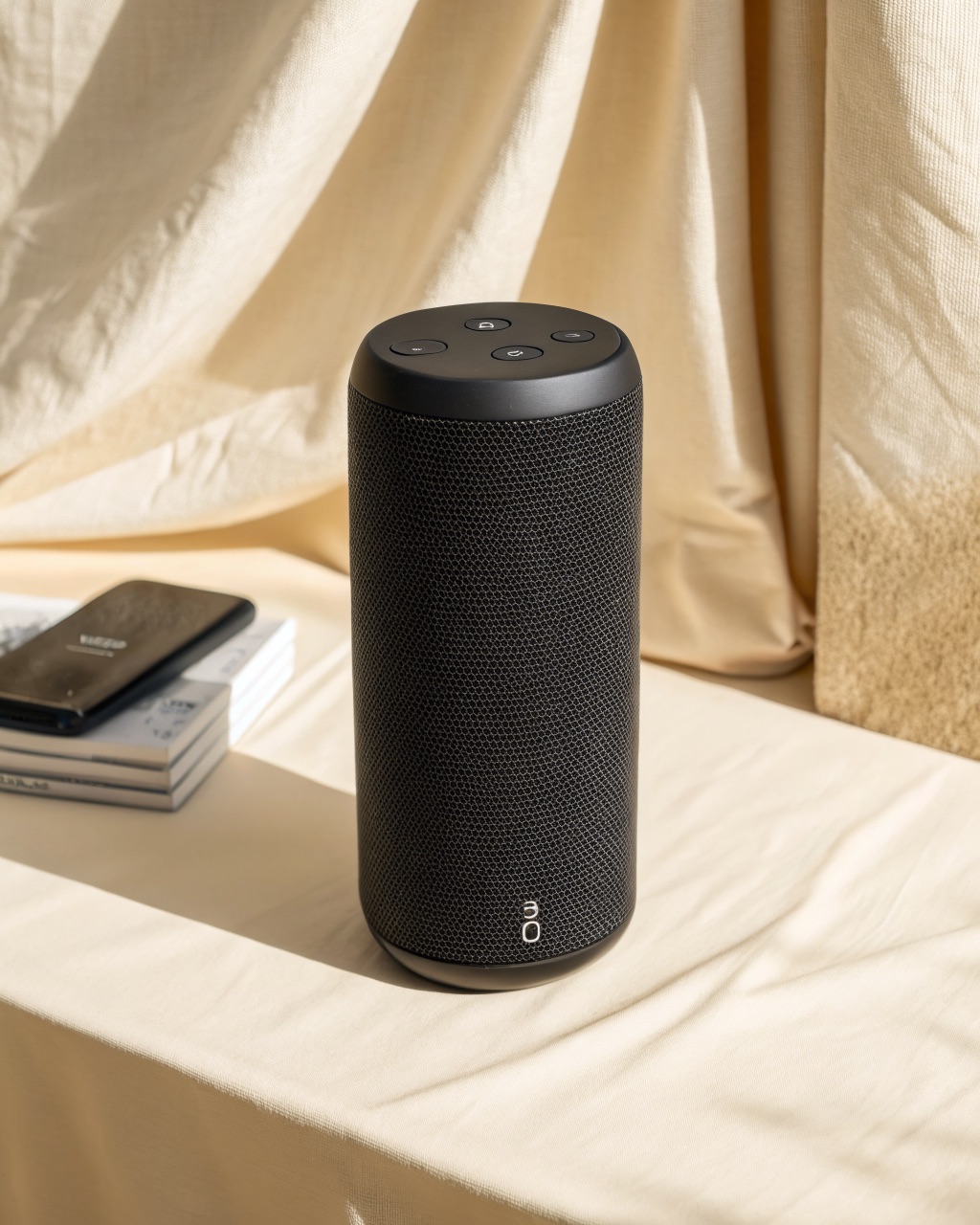 Cylindrical Bluetooth speaker standing upright, showing the fabric-wrapped driver circumference