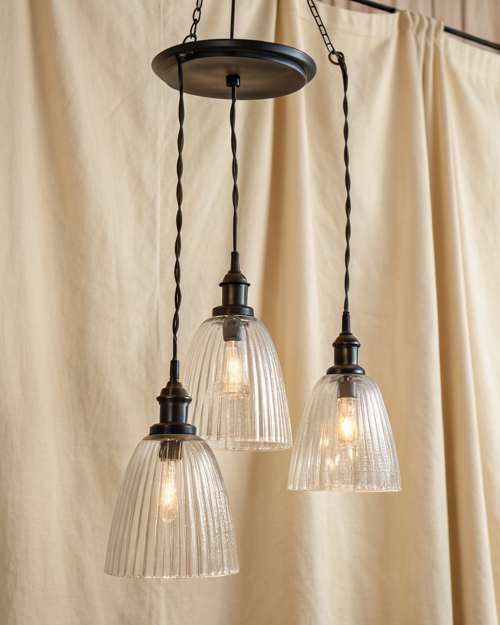 Three ribbed clear-glass bell pendants hanging in a row at staggered heights from a single black rectangular ceiling canopy