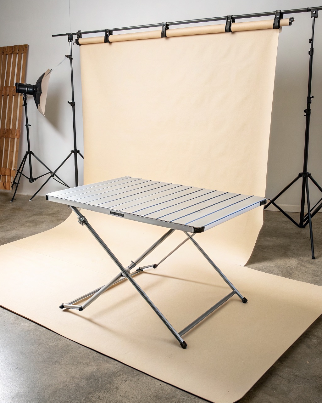 Anodized aluminum camp table set up on grass with a roll-up slatted top and folding tube legs, carry bag beside it