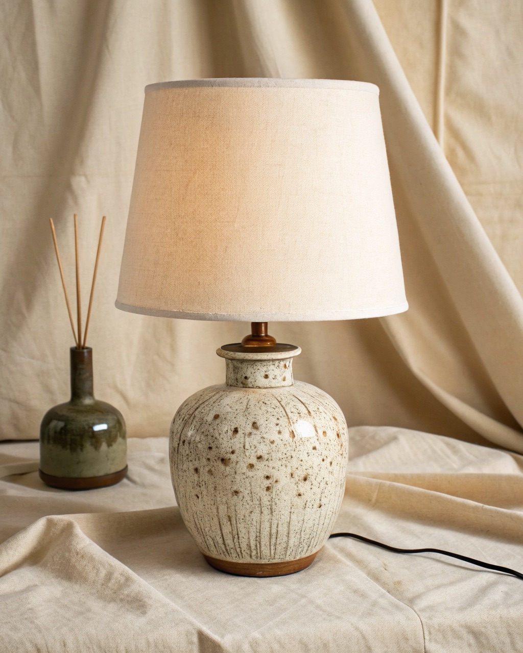 Small glazed ceramic bedside lamp with a speckled reactive glaze and a natural cotton drum shade