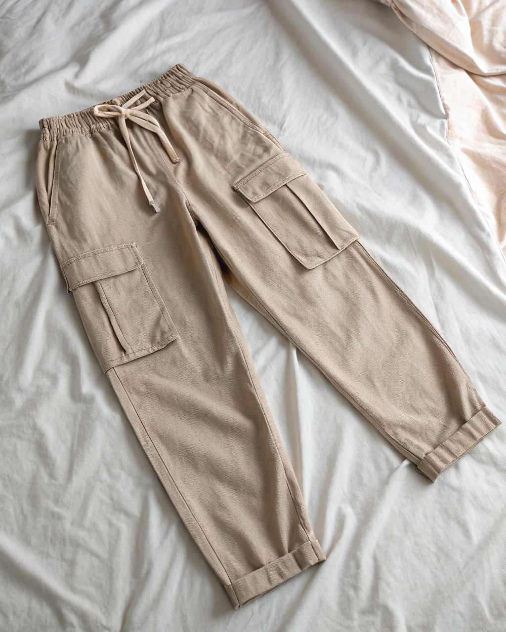 Stone linen-cotton utility trousers laid flat with a drawstring waist and a single thigh cargo pocket