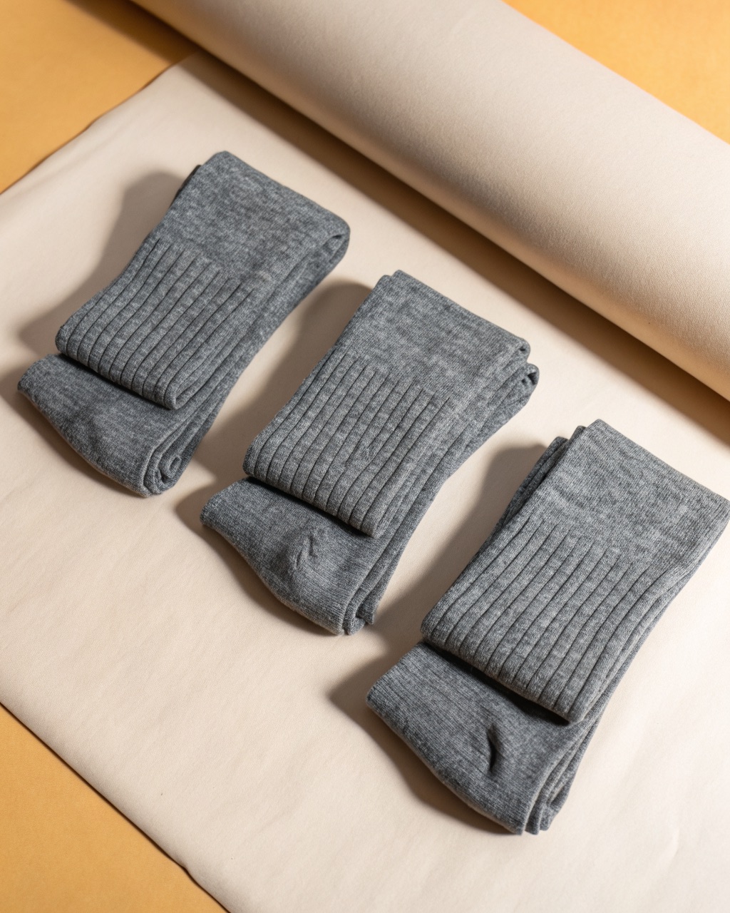 Three pairs of grey merino crew socks folded and stacked, showing ribbed cuffs and cushioned soles