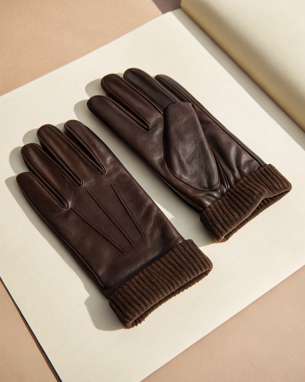 Pair of dark brown oiled leather gloves laid flat with ribbed knit cuffs and inside seams