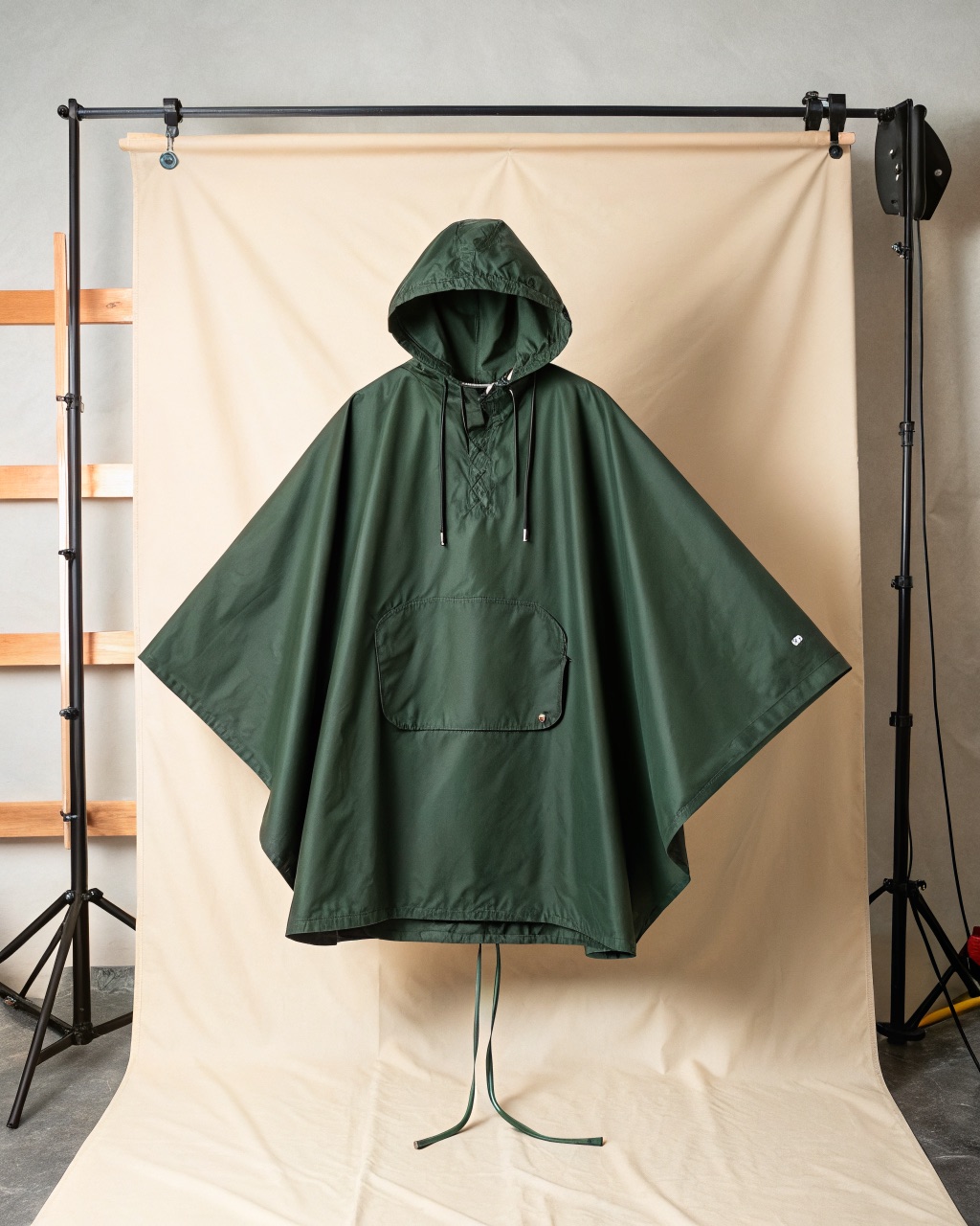 Forest green hooded rain poncho laid flat showing the stiffened hood brim, side snaps, and corner tarp loops, with its stuff pocket beside it