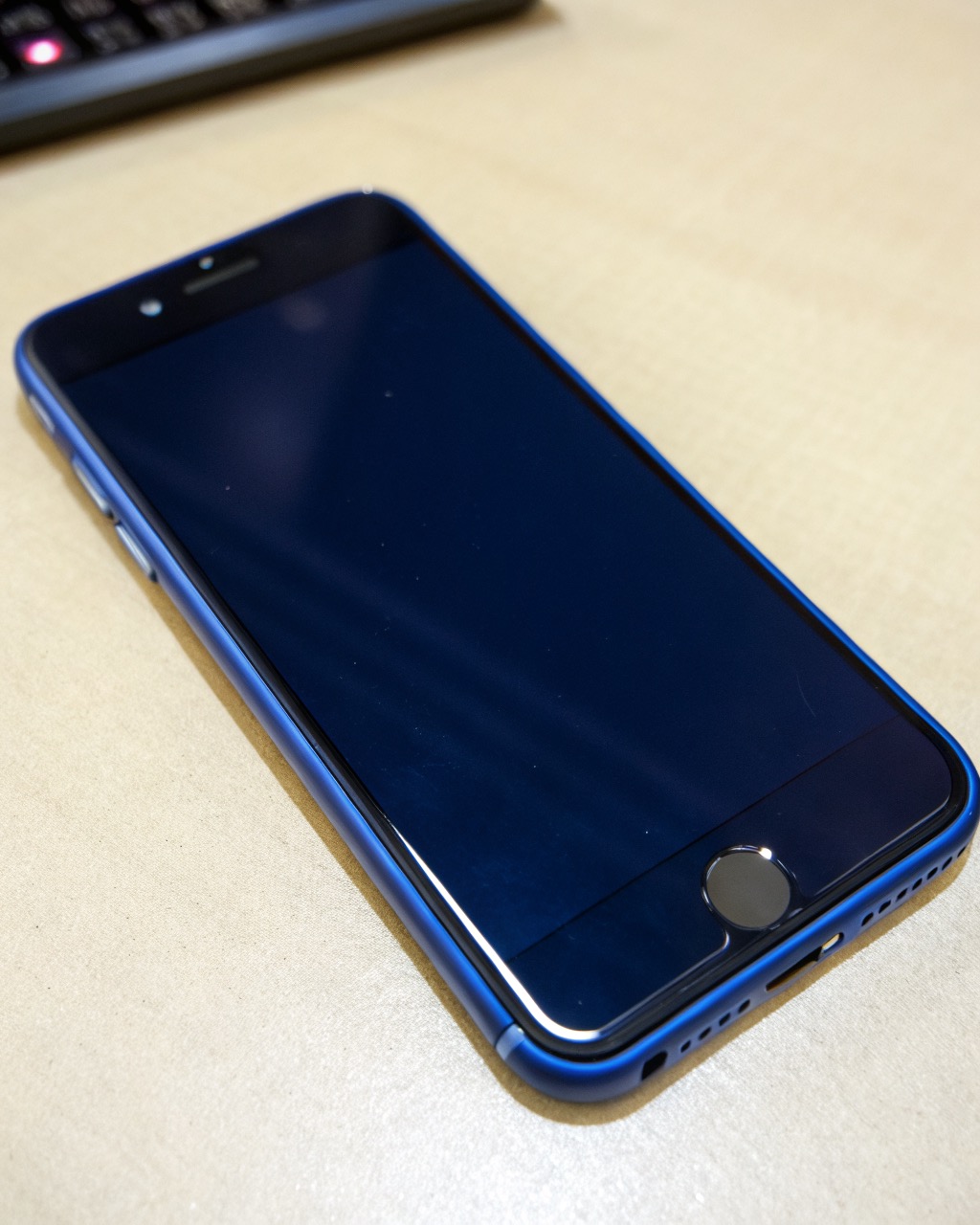 Deep-blue smartphone shown back-first with a large square camera island containing a prominent periscope telephoto lens, angled view, no branding