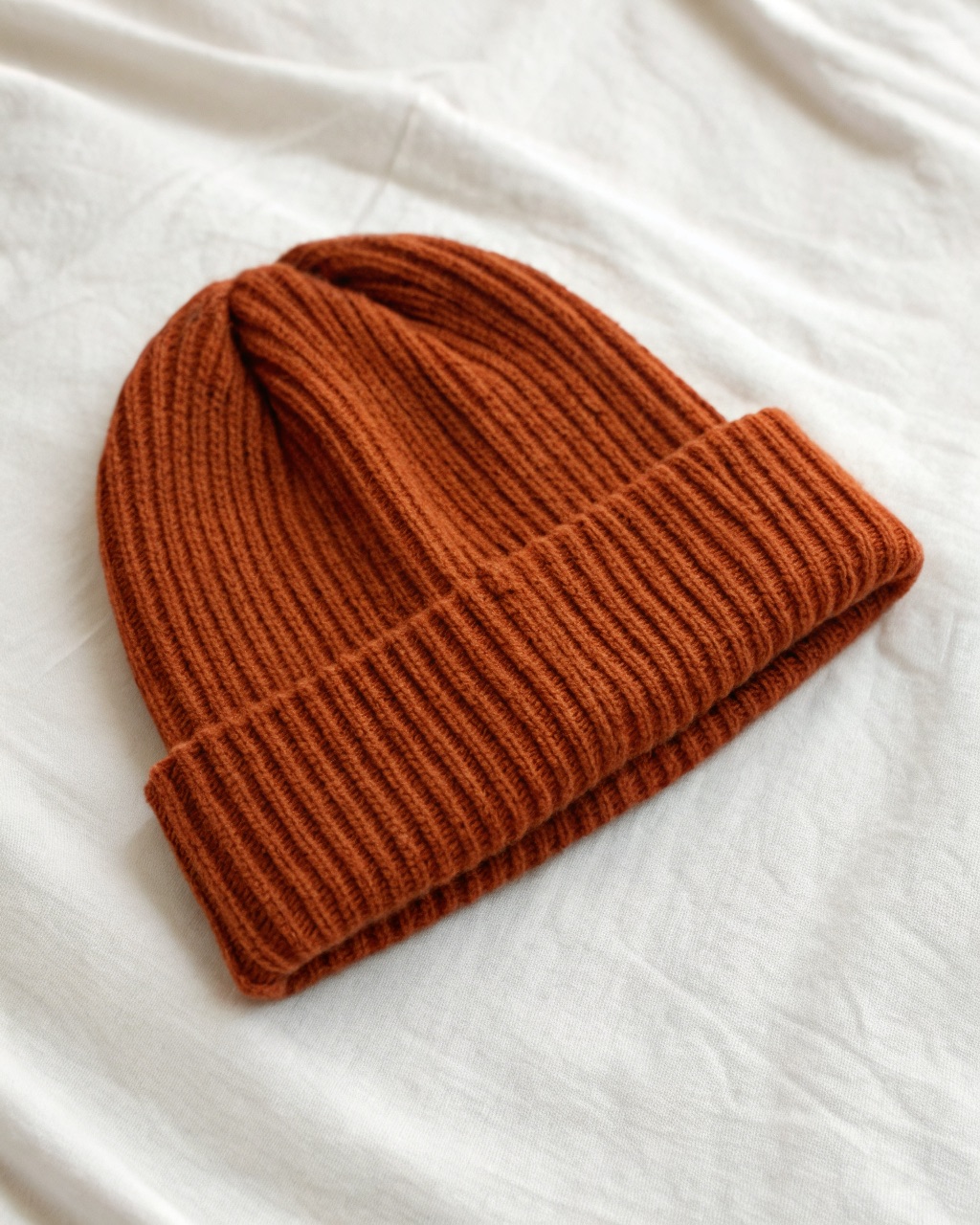 Rust-colored long ribbed beanie laid flat showing the deep 4x2 rib knit and folded cuff