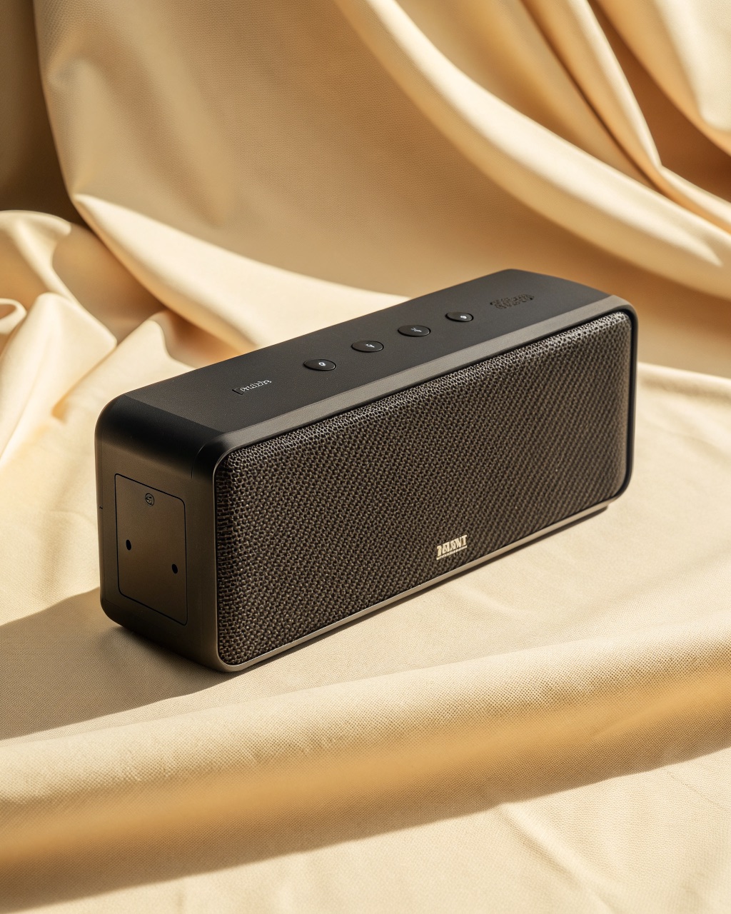 Flat rectangular Bluetooth speaker with a grey woven fabric front face and a black rubber strap on the back