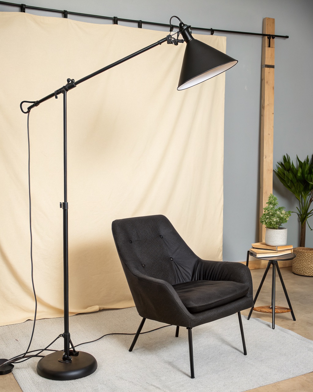 Tall black floor lamp with a horizontal swing arm and a conical steel task shade angled over a reading chair