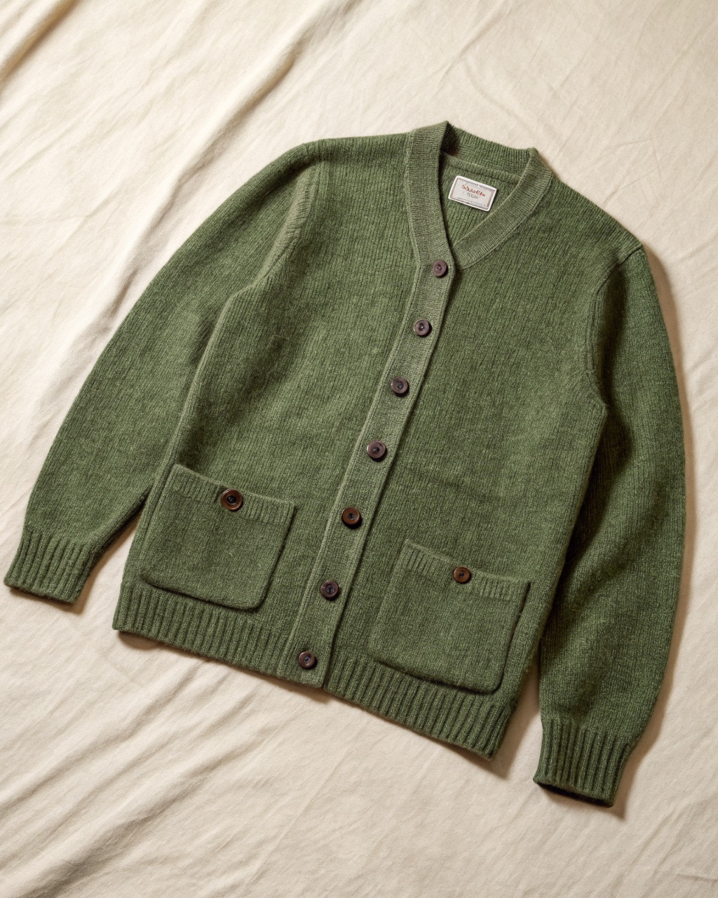 Moss-heather Shetland wool cardigan laid flat with five leather buttons and two waist patch pockets