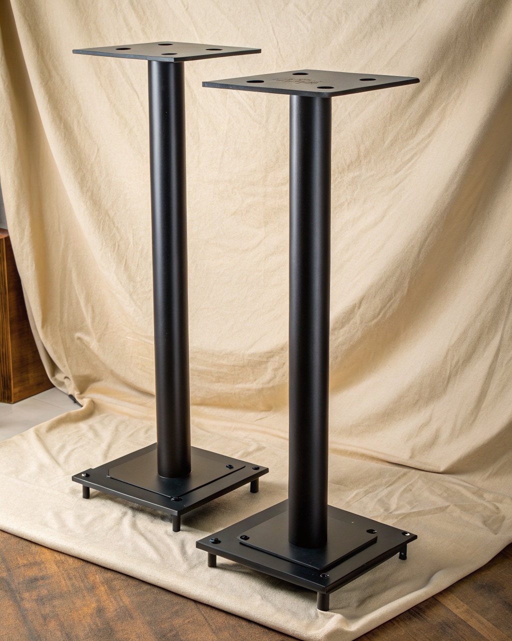 Pair of satin black steel speaker stands with square top plates and a single fillable central column on a wide base with spikes