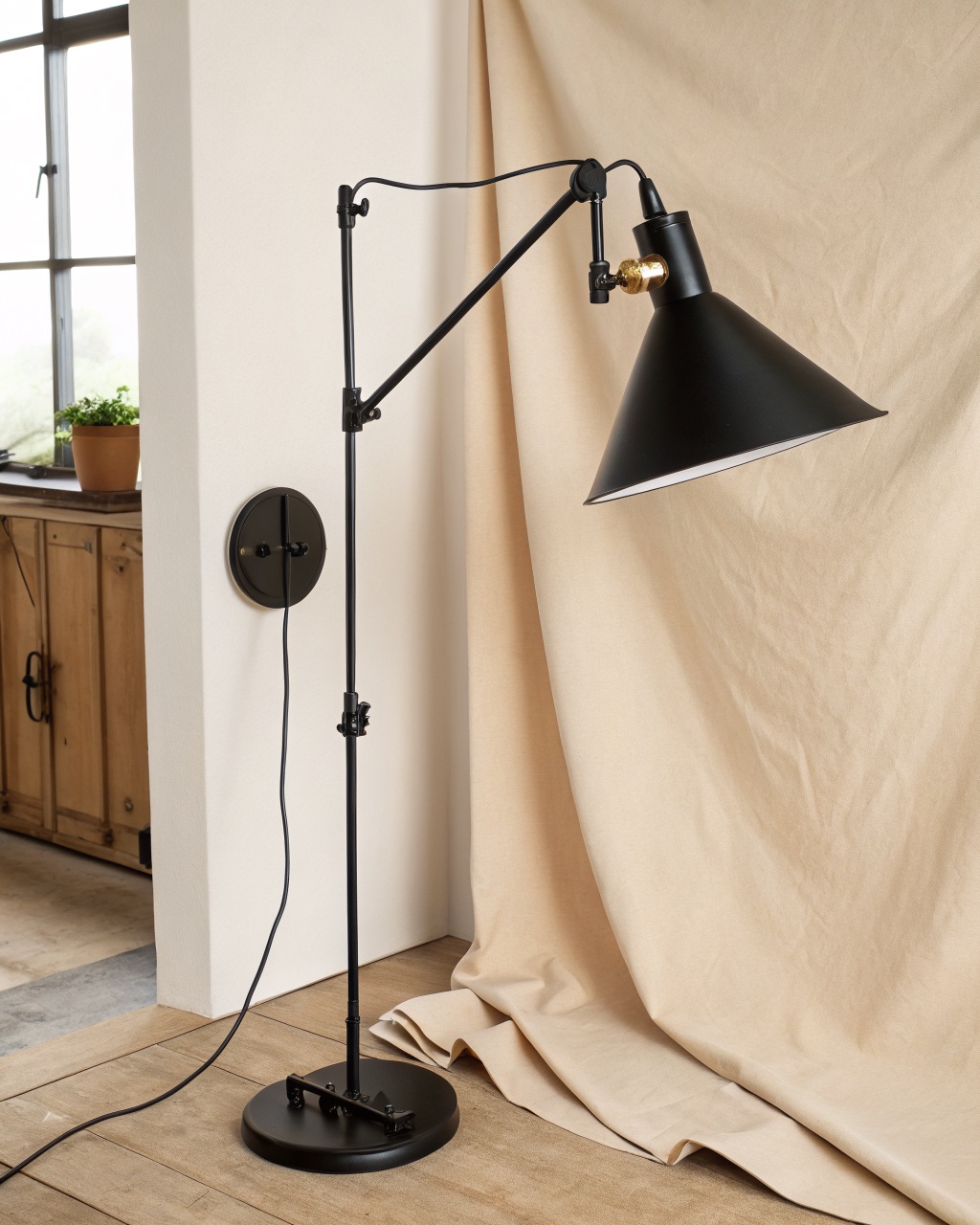 Plug-in black steel swing-arm wall lamp with a folding two-section arm and a tilting cone shade mounted beside a chair