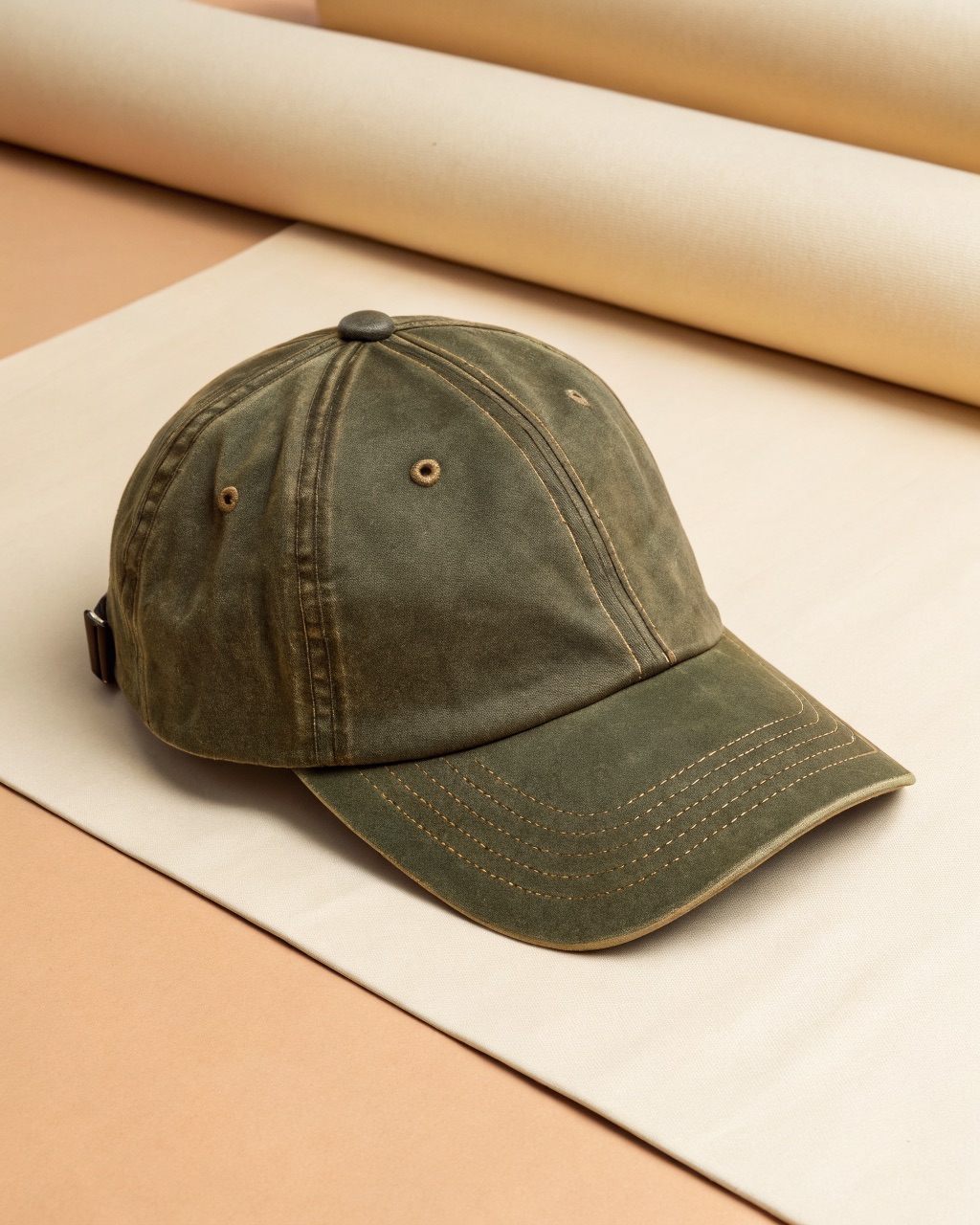 Olive waxed cotton six-panel cap laid flat with curved brim and brass rear slider visible